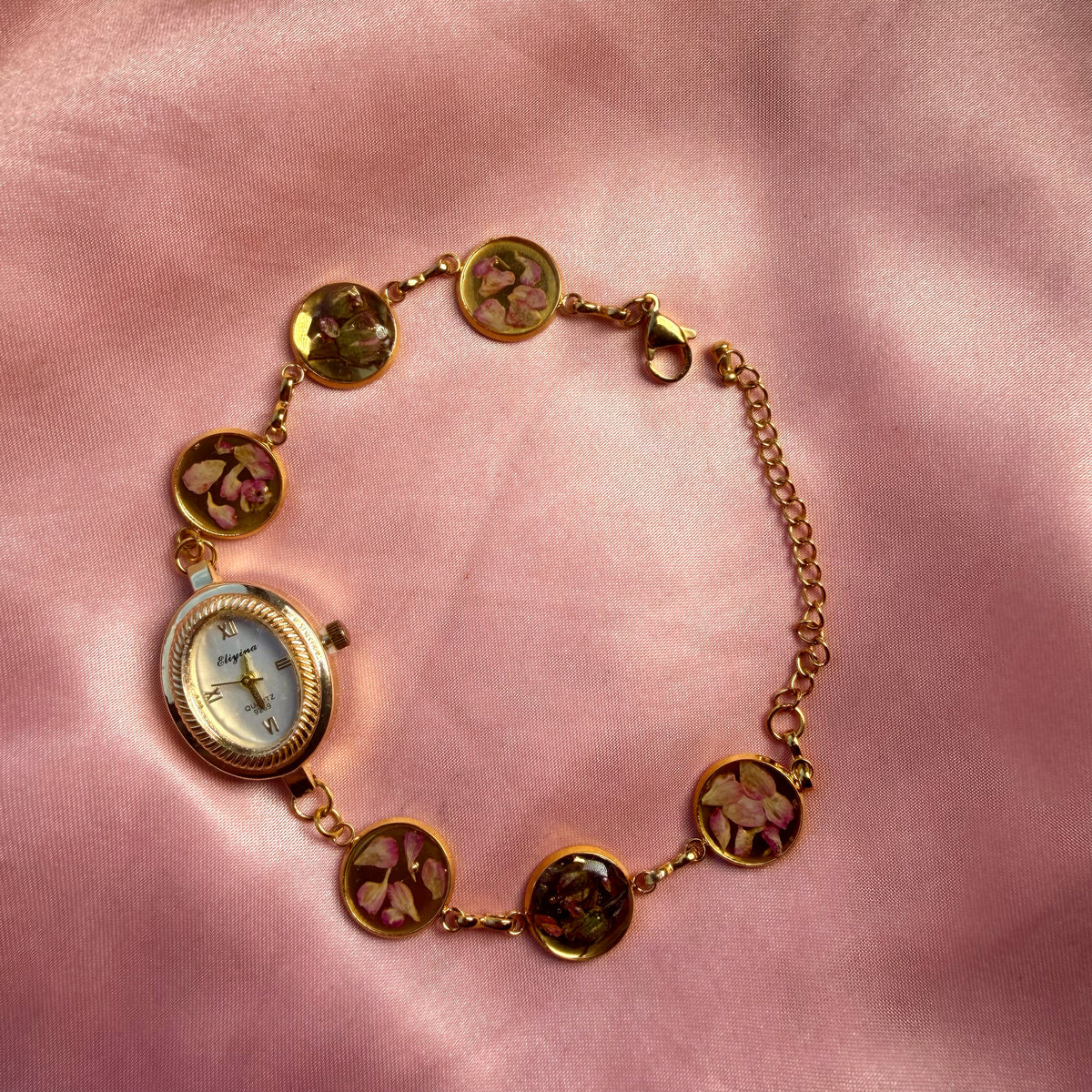 A gold-tone oval bracelet watch with a pale dial and a handmade floral band