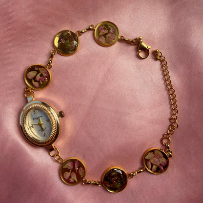 Close-up of gold-tone oval bracelet watch with a pale dial and a handmade floral band