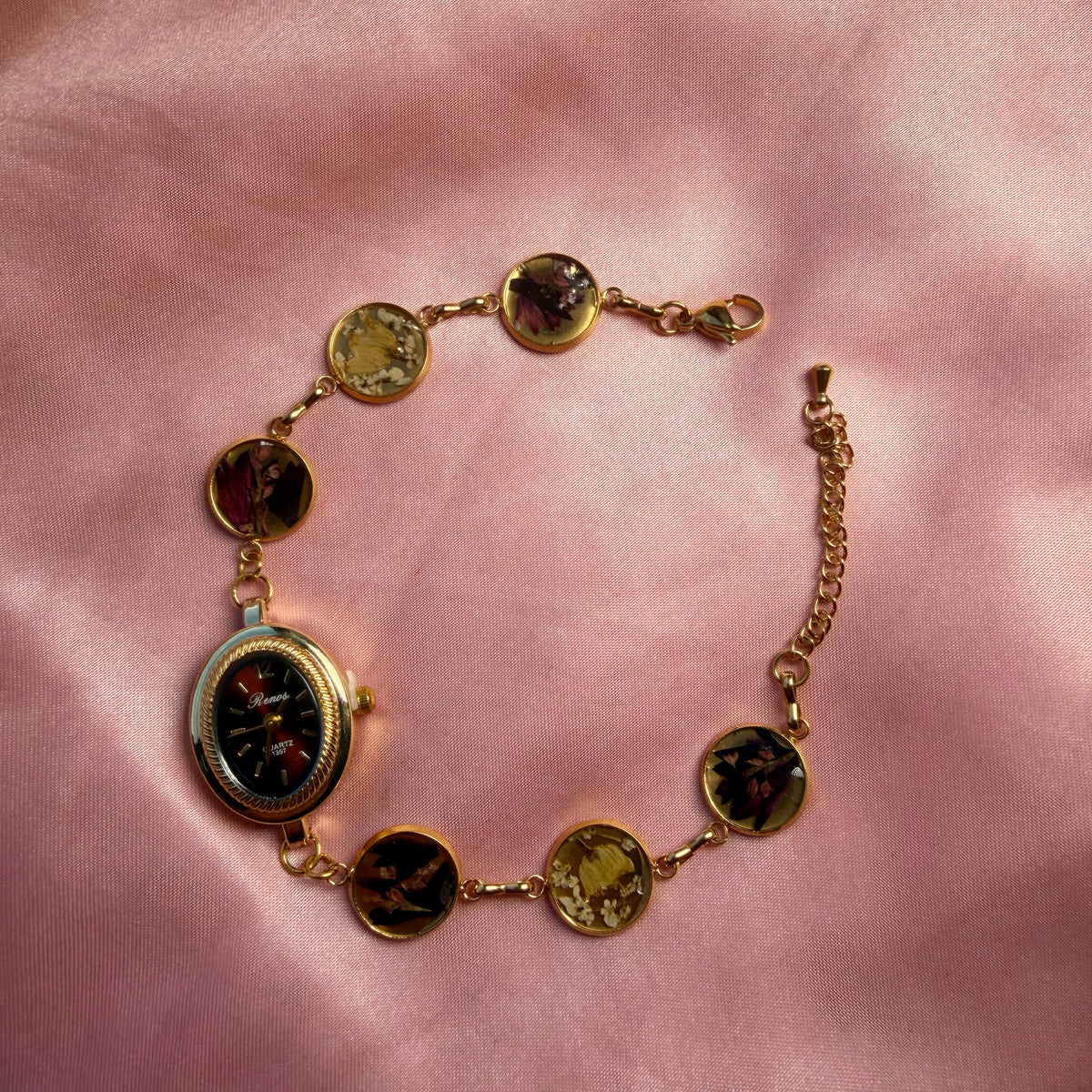 A gold-tone oval bracelet with a dark dial and a handmade floral band