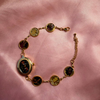 A gold-tone oval bracelet with a dark dial and a handmade floral band