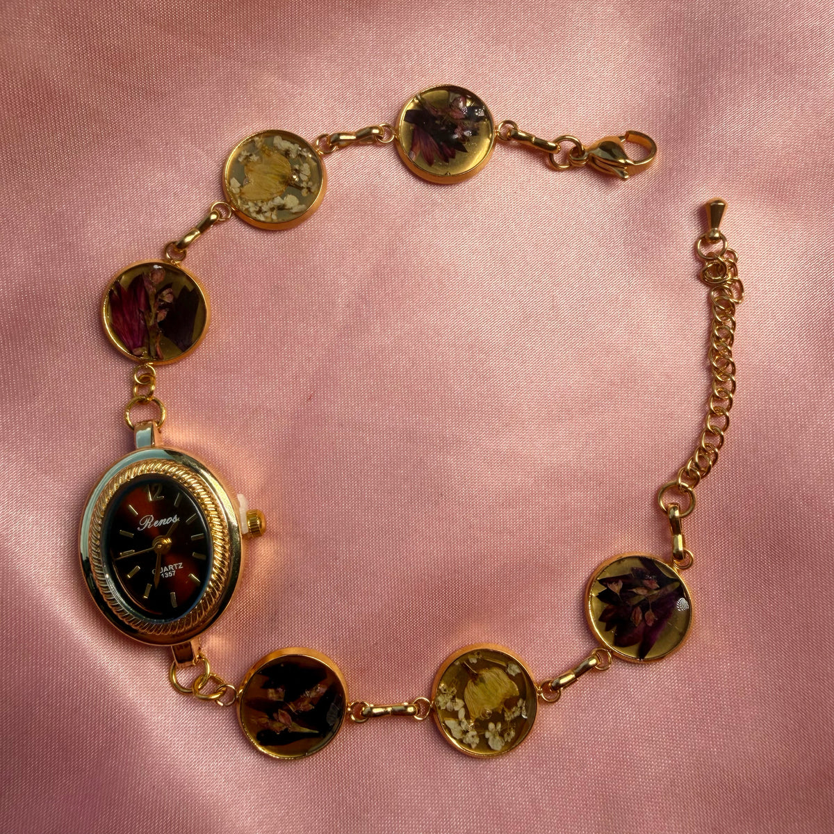 Close-up of gold-tone oval bracelet with a dark dial and a handmade floral band