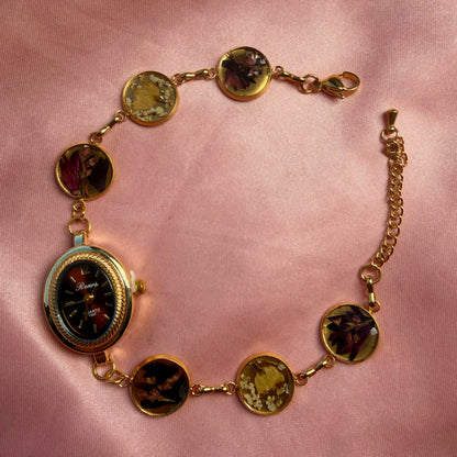 Close-up of gold-tone oval bracelet with a dark dial and a handmade floral band