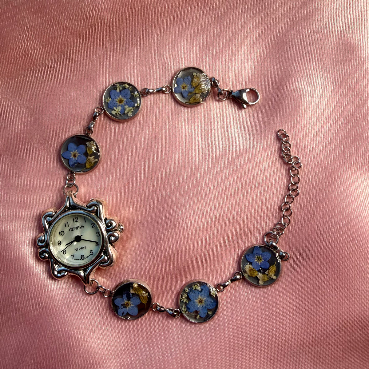 A silver-tone bracelet with an ornate oval face and a handmade floral band