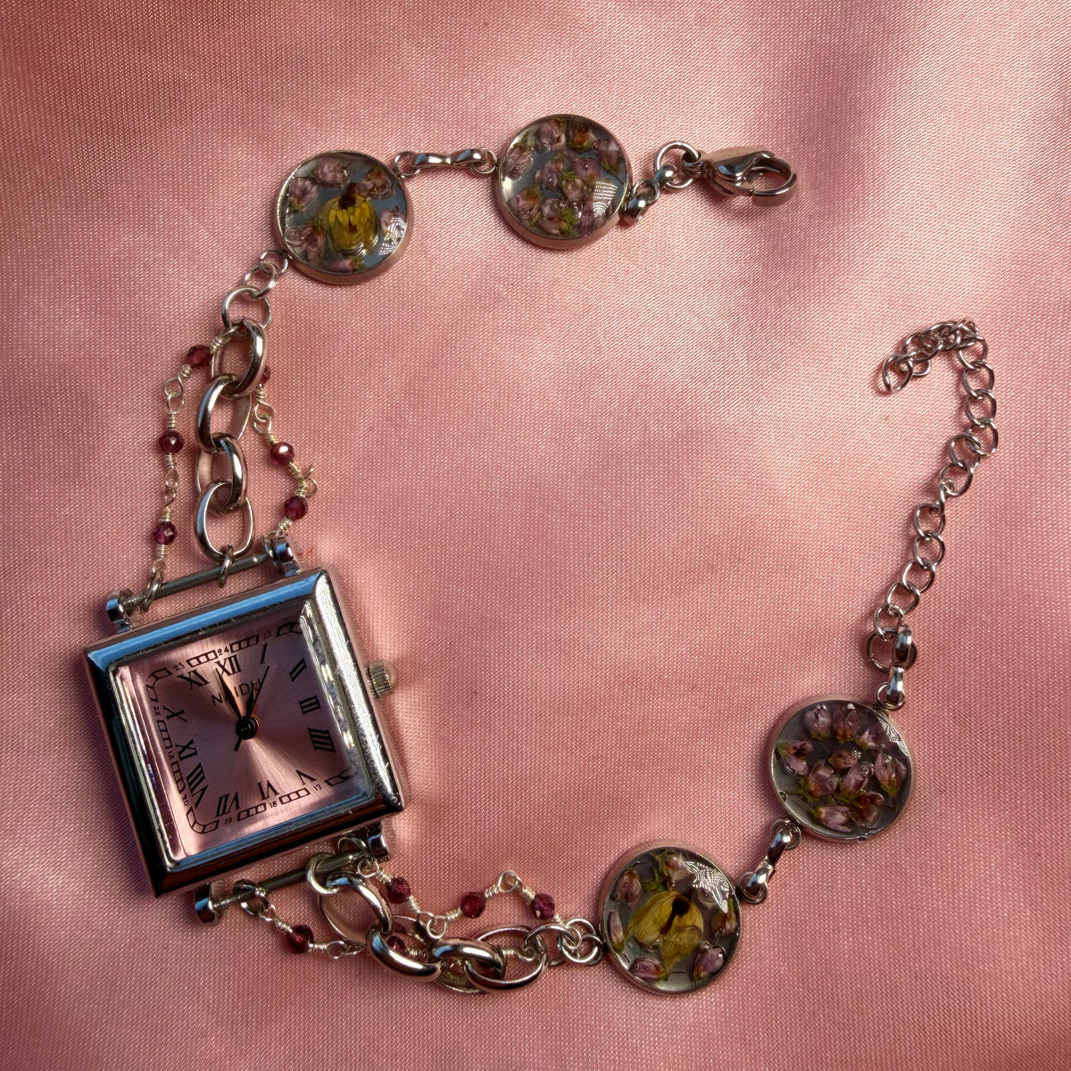 Close-up of silver-tone bracelet with a square pink dial and a handmade floral band