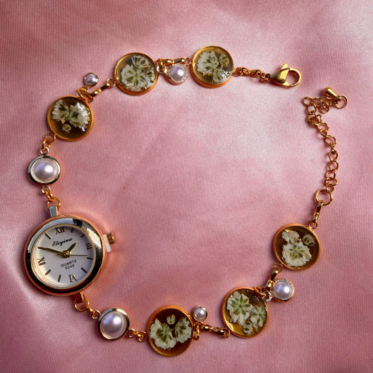 A gold-tone round bracelet with a pale dial and a handmade floral band