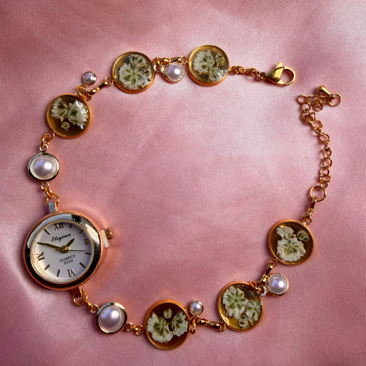 Close-up of gold-tone round bracelet with a pale dial and a handmade floral band
