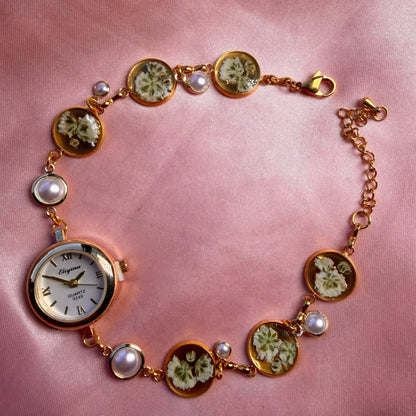 Close-up of gold-tone round bracelet with a pale dial and a handmade floral band