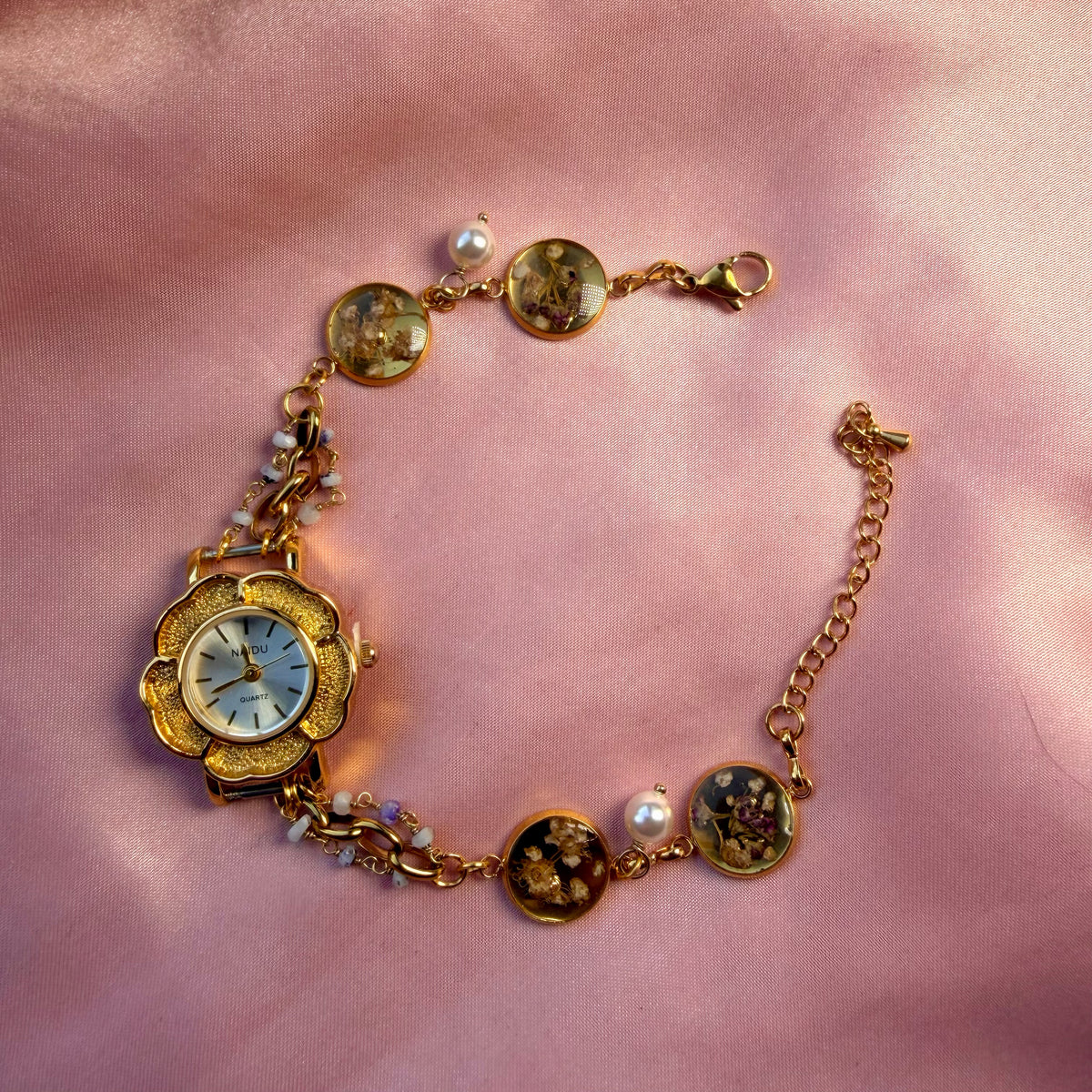 A gold-tone flower-shaped bracelet with a pale dial and a handmade floral band