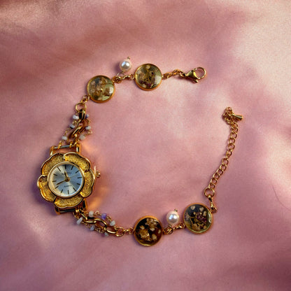 A gold-tone flower-shaped bracelet with a pale dial and a handmade floral band