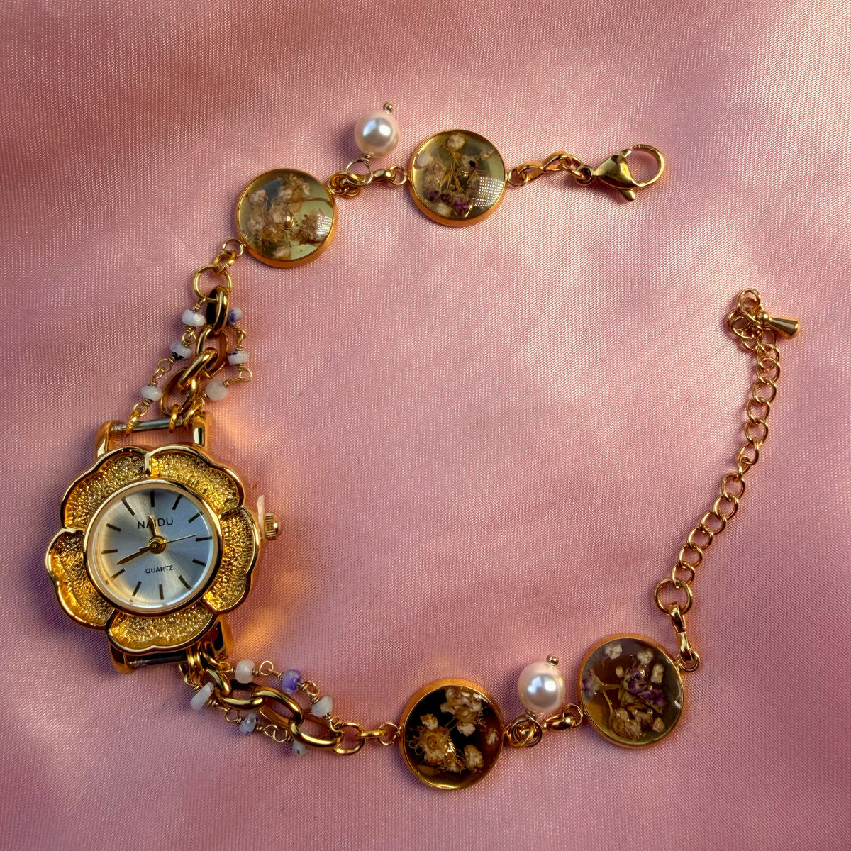 Close-up of gold-tone flower-shaped bracelet with a pale dial and a handmade floral band