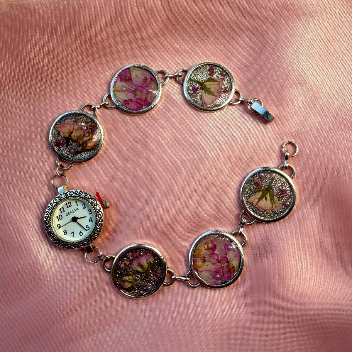 A silver-tone bracelet with an ornate round face and a handmade floral band